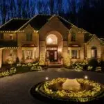 Brick estate with a complete warm-white roofline and illuminated landscape installation