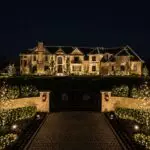 Vertical view through an illuminated gate toward a roofline-lit estate